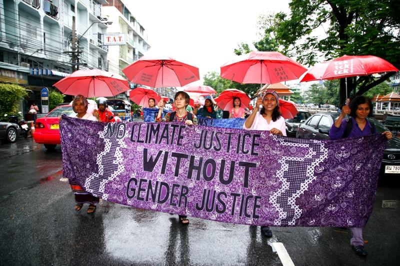 Ein Demonstrationszug. Vier Personen halten ein lila Transparent. Darauf steht "no climate justice without gender justice"