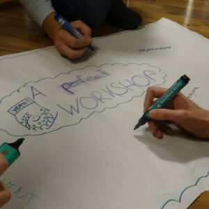 Drei Hände schreiben auf ein Flipchart. Darauf steht "A potential workshop"