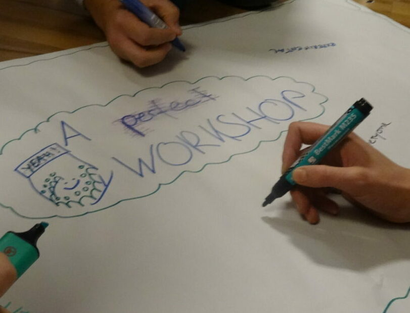 Drei Hände schreiben auf ein Flipchart. Darauf steht "A potential workshop"